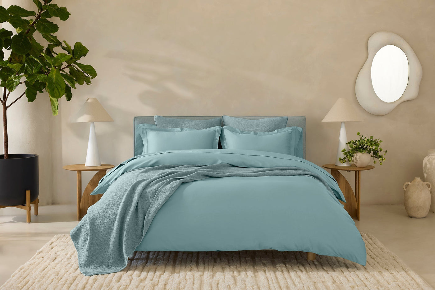 Sage blue sateen duvet cover and pillows styled on a bed in a warm neutral bedroom.