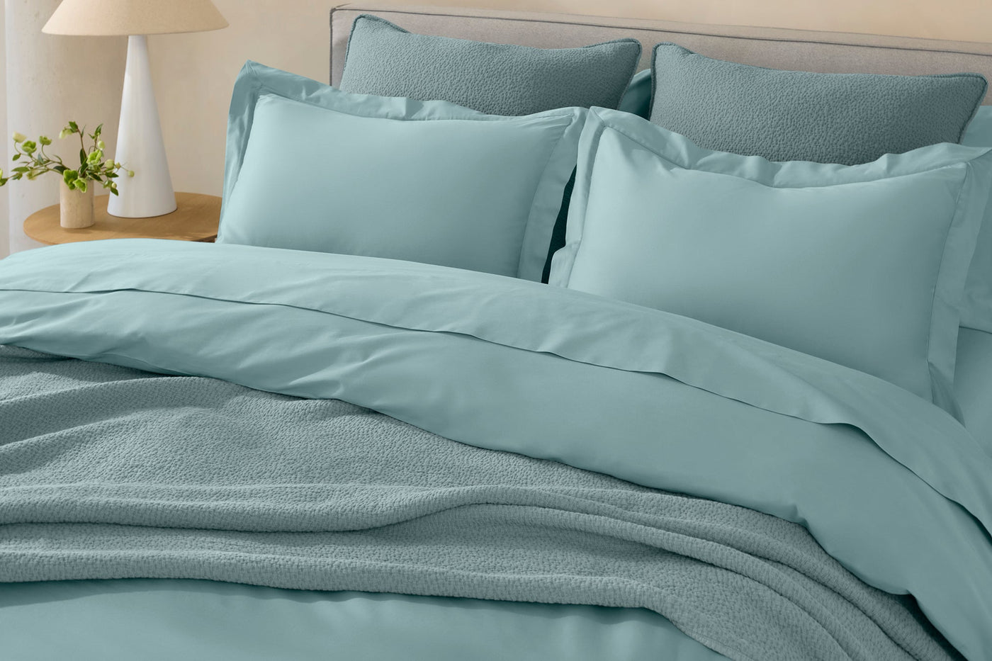 Close-up of Coyuchi Cloud Soft Sateen duvet cover in seafoam with textured blanket layered at foot.