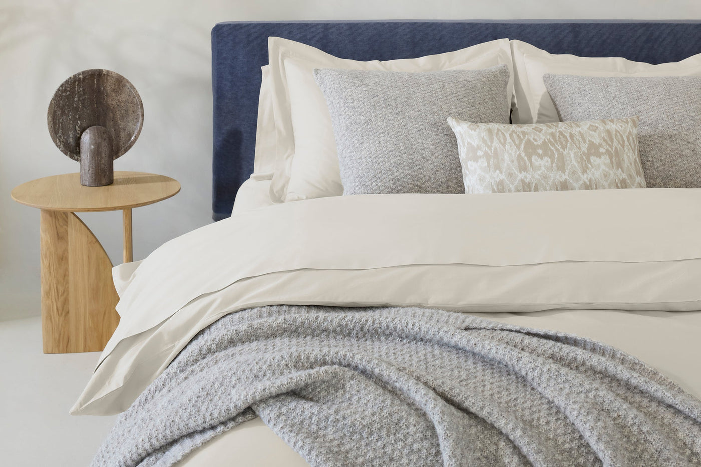 Ivory sateen duvet cover styled with blue-patterned pillows and a grey knit throw.