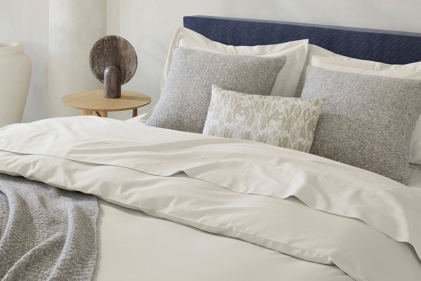 Ivory sateen duvet cover styled on bed with layered grey textured pillows and navy headboard.