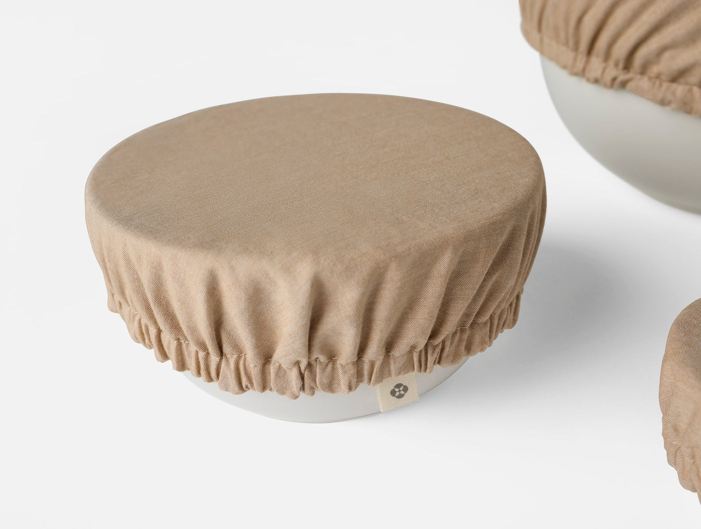 Camel-toned linen bowl cover with gathered elastic edge fitted over a white ceramic bowl.