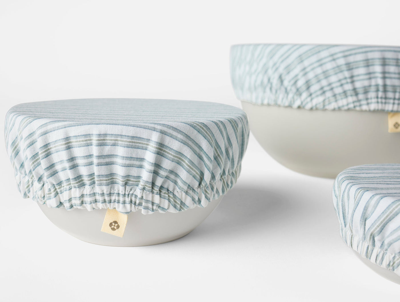 Coyuchi Conserve bowl covers in blue stripe linen, elasticated edges shown on three ceramic bowls.