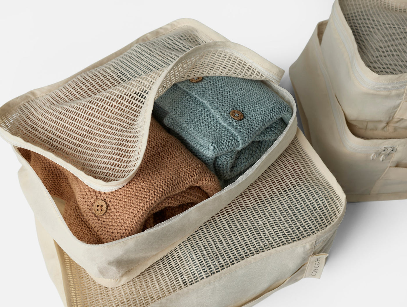 Coyuchi Conserve packing cubes open, showing folded knit garments in terracotta and slate blue.
