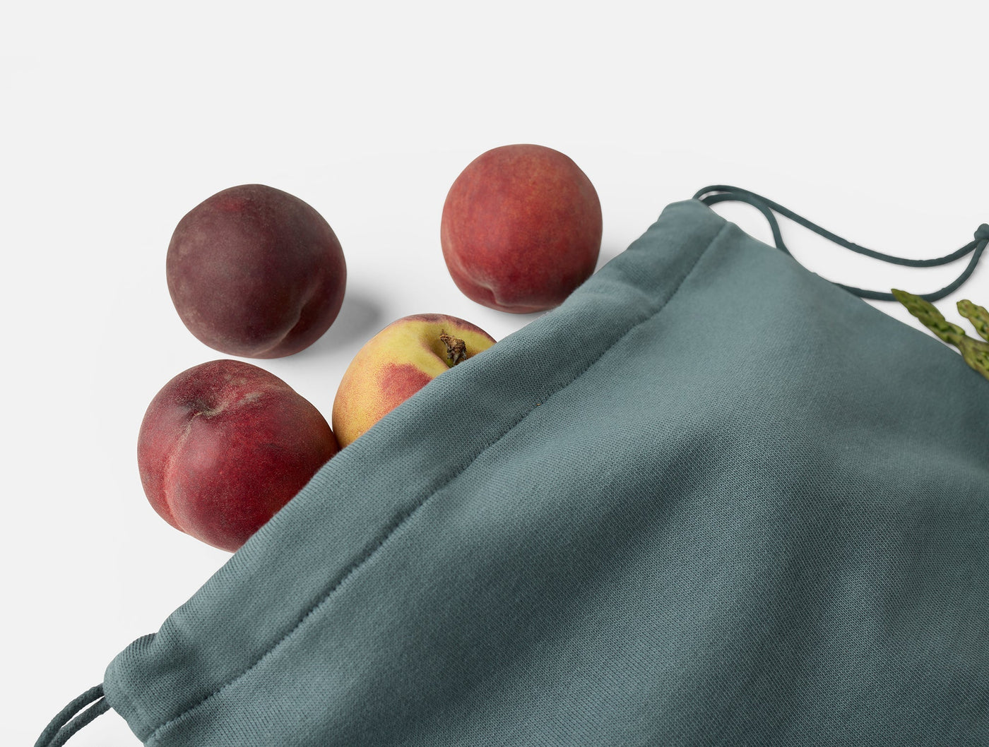 Sage green Coyuchi drawstring produce bag with peaches spilling out, close-up detail.