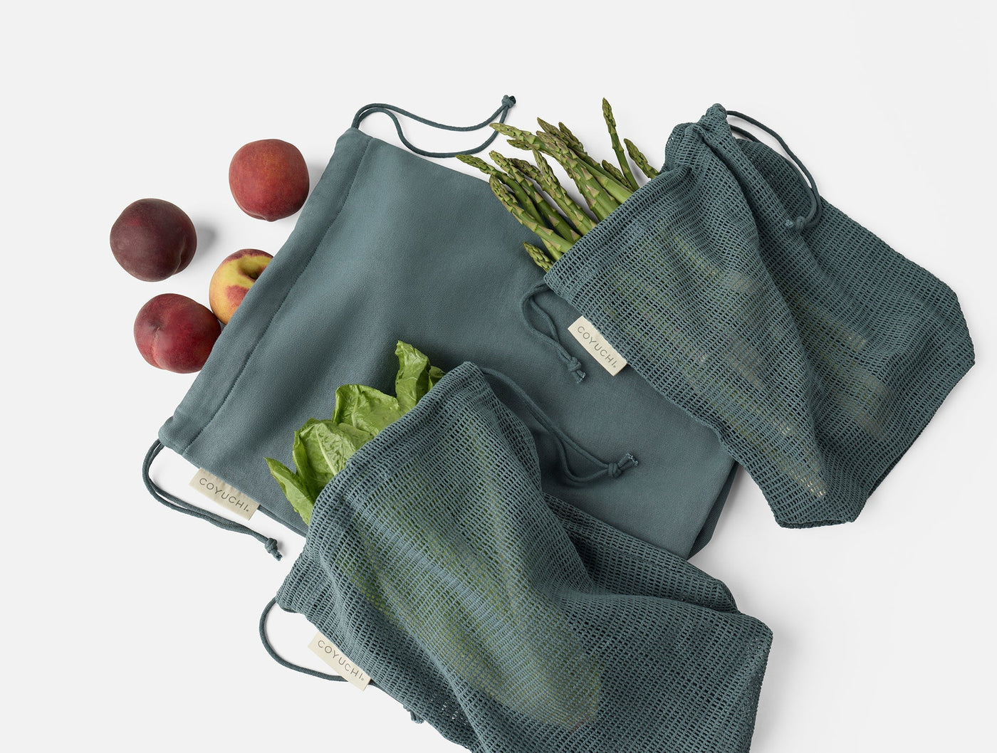 Coyuchi Conserve produce bag set in slate, styled with fresh peaches and vegetables.