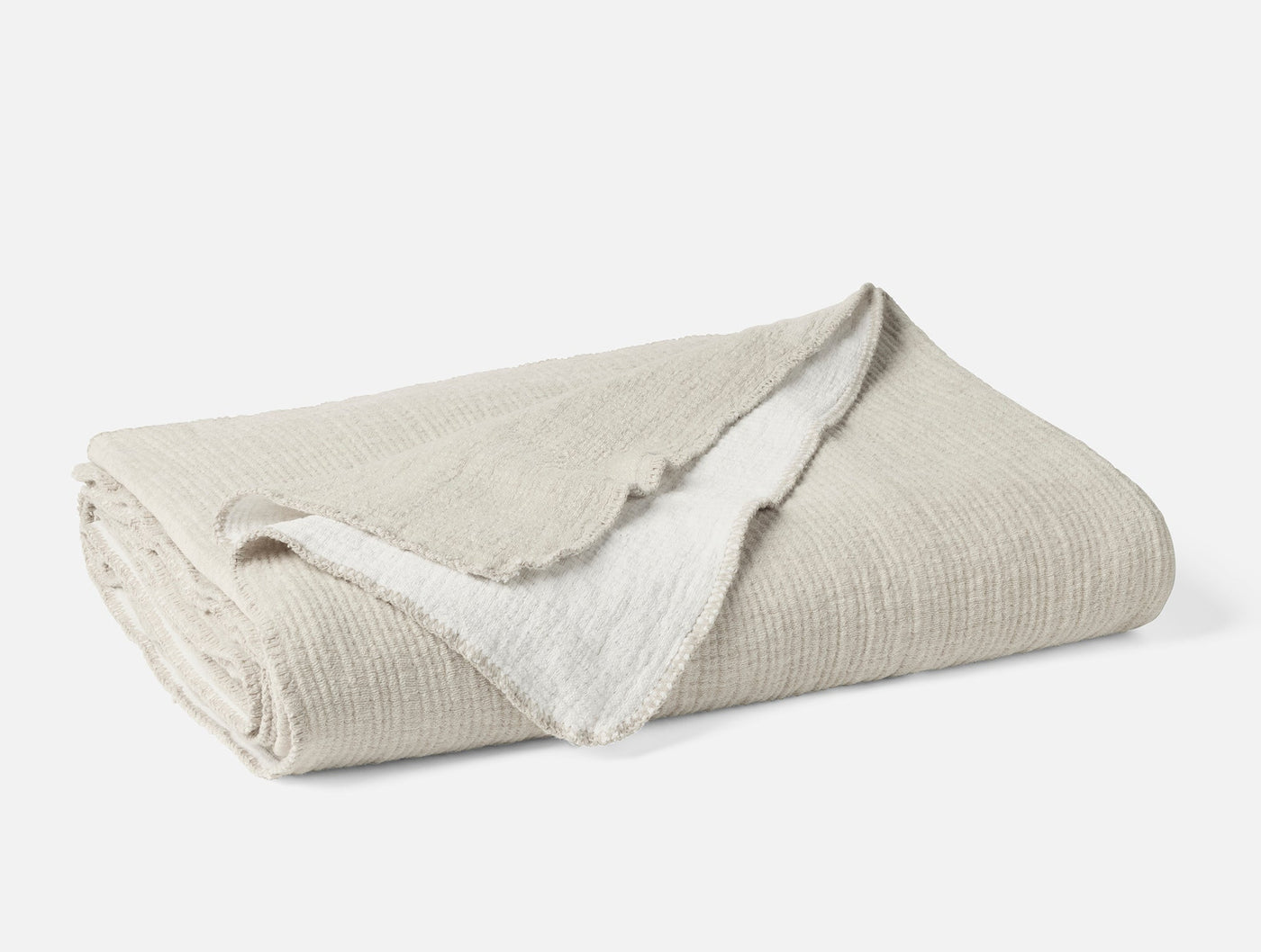 Folded ivory Coyuchi Cozy Cotton blanket showing textured weave and contrast white reverse.