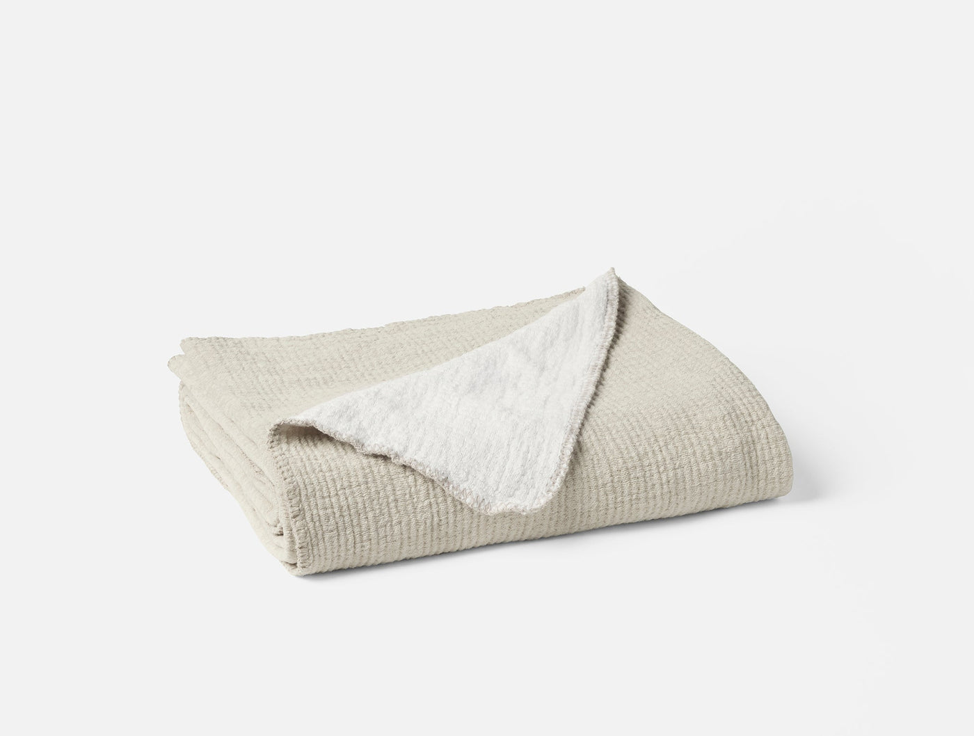 Folded Coyuchi Cozy Cotton Throw showing oatmeal waffle-textured front and white sherpa reverse.
