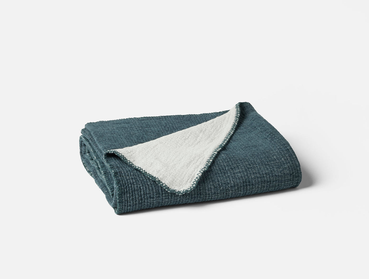 Folded teal throw with textured waffle weave exterior and ivory reverse, corner turned back.