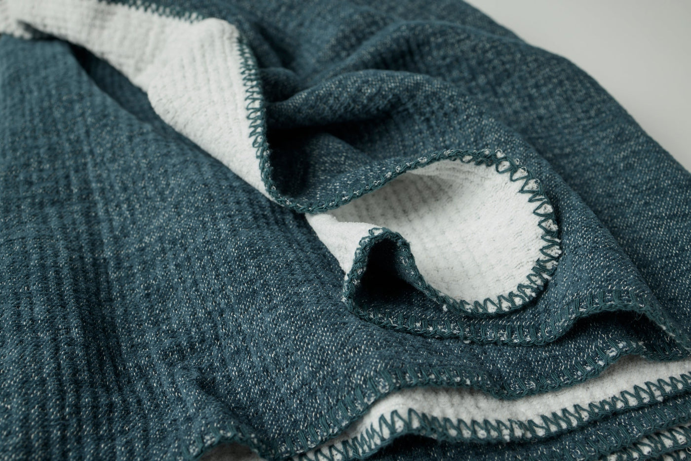 Close-up of Coyuchi Cozy Cotton Throw hem, showing teal herringbone weave and contrast blanket stitching.