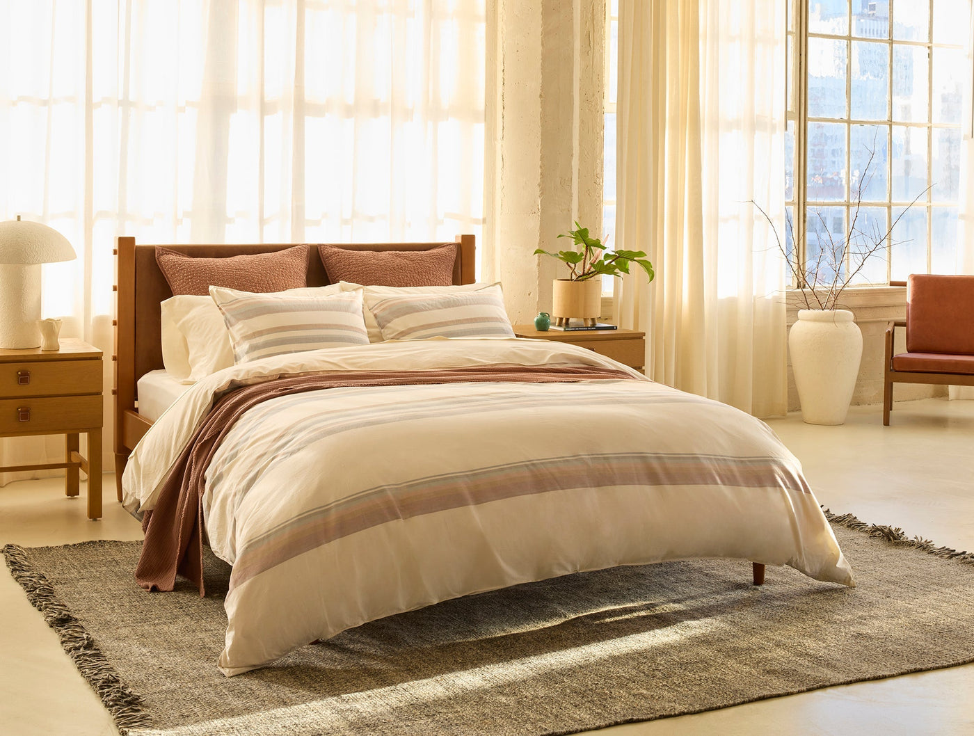 Ivory striped duvet and shams styled on a wood-framed bed in a warm, sunlit bedroom.