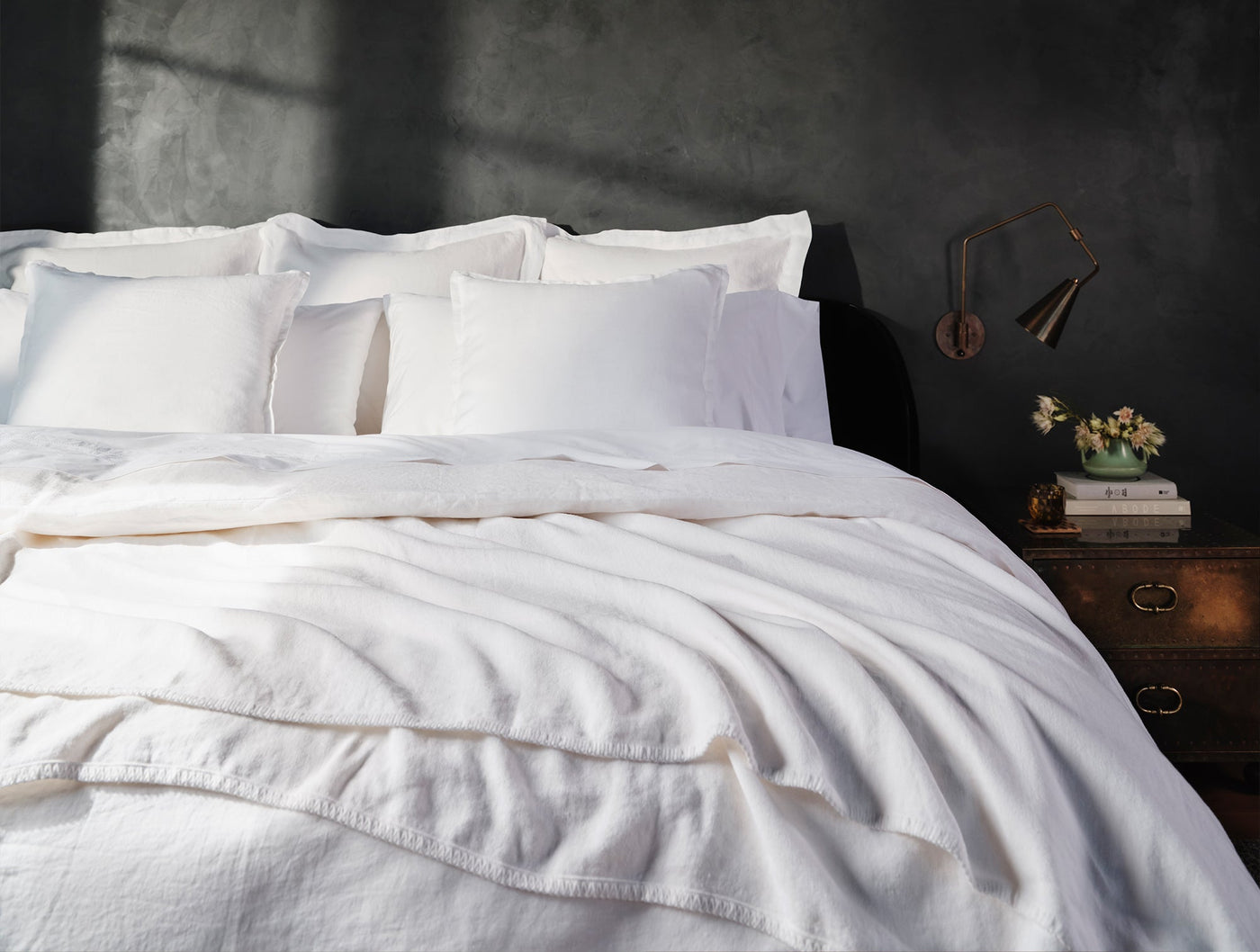 Coyuchi Relaxed Linen white sheets and duvet styled on bed against dark moody wall.