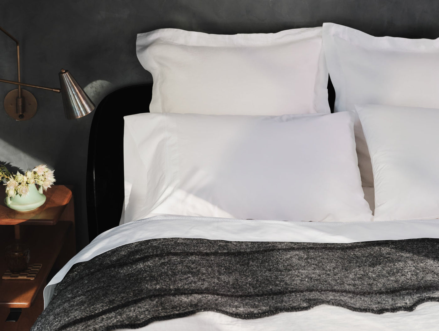 White Coyuchi Relaxed Linen sheet set on dark-framed bed with charcoal throw blanket.