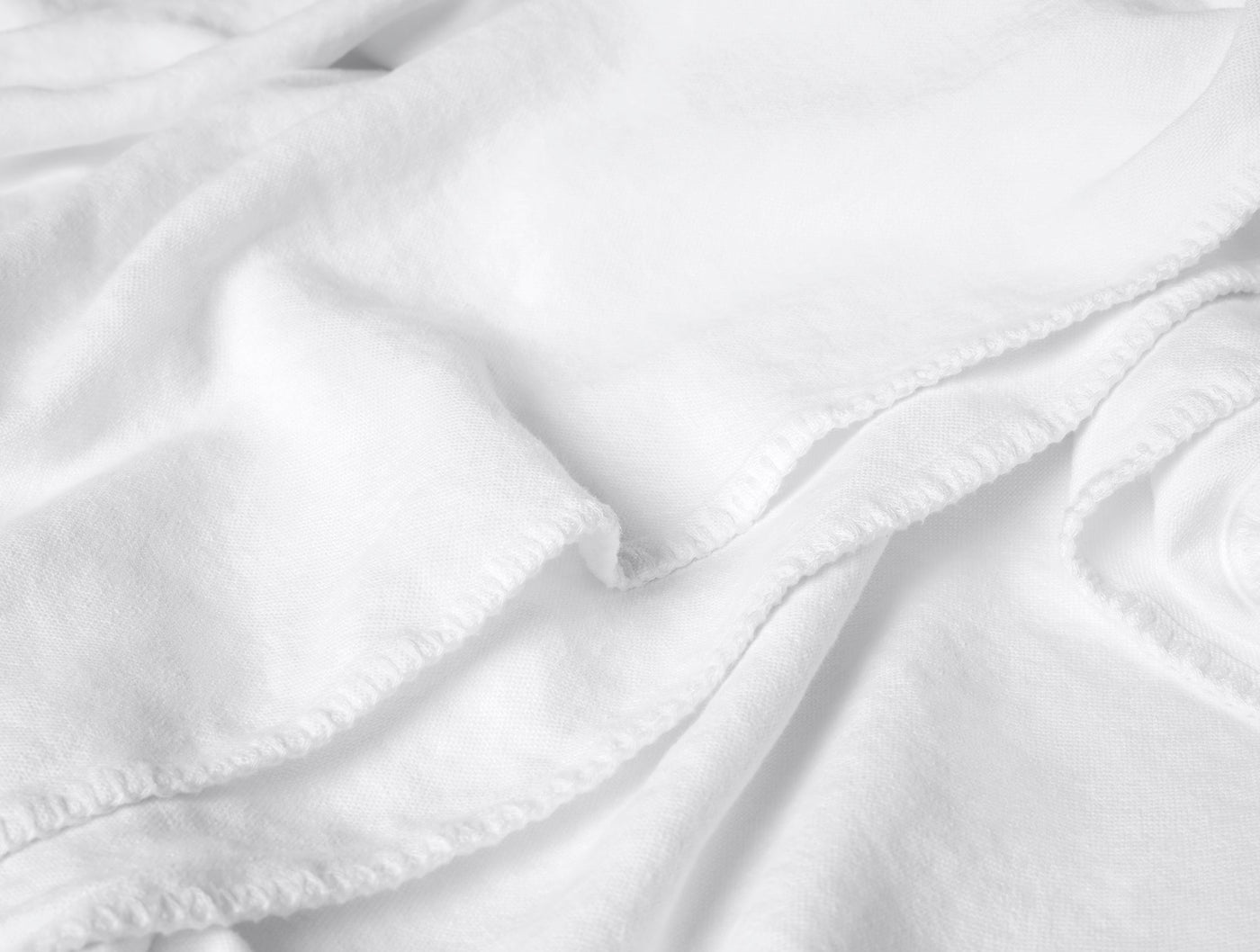 Close-up of white linen blanket showing soft drape and blanket stitch trim detail.