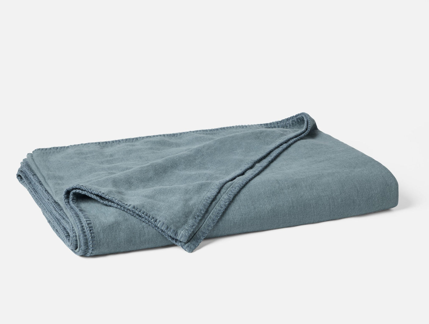 Close-up of folded Coyuchi Helena Linen blanket in slate blue, showing blanket stitch edge trim.