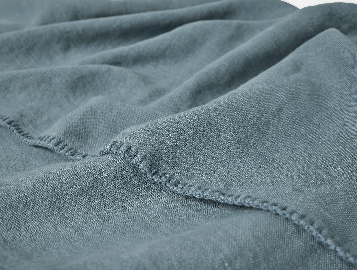 Close-up of slate blue linen blanket showing blanket stitch hem detail and soft drape.