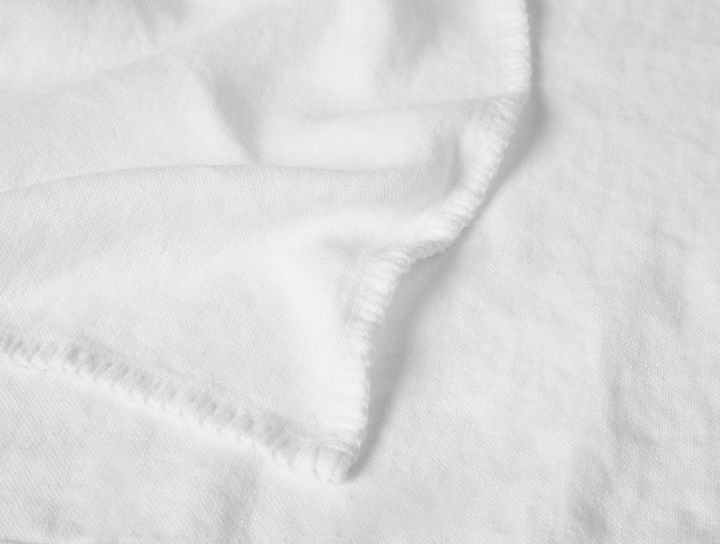 Close-up of white linen blanket corner showing blanket stitch edge detail and soft drape.