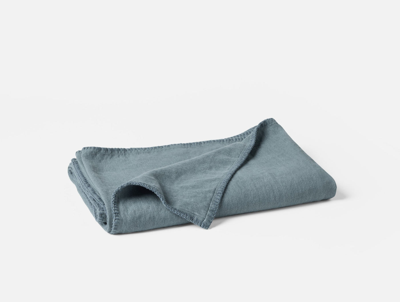 Folded slate blue linen throw, corner turned back to show texture and blanket-stitched edge.