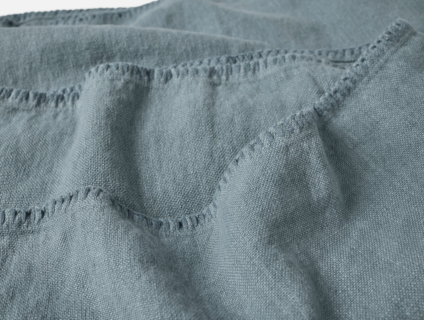Close-up of slate blue linen blanket showing frayed edge hem detail and woven texture.