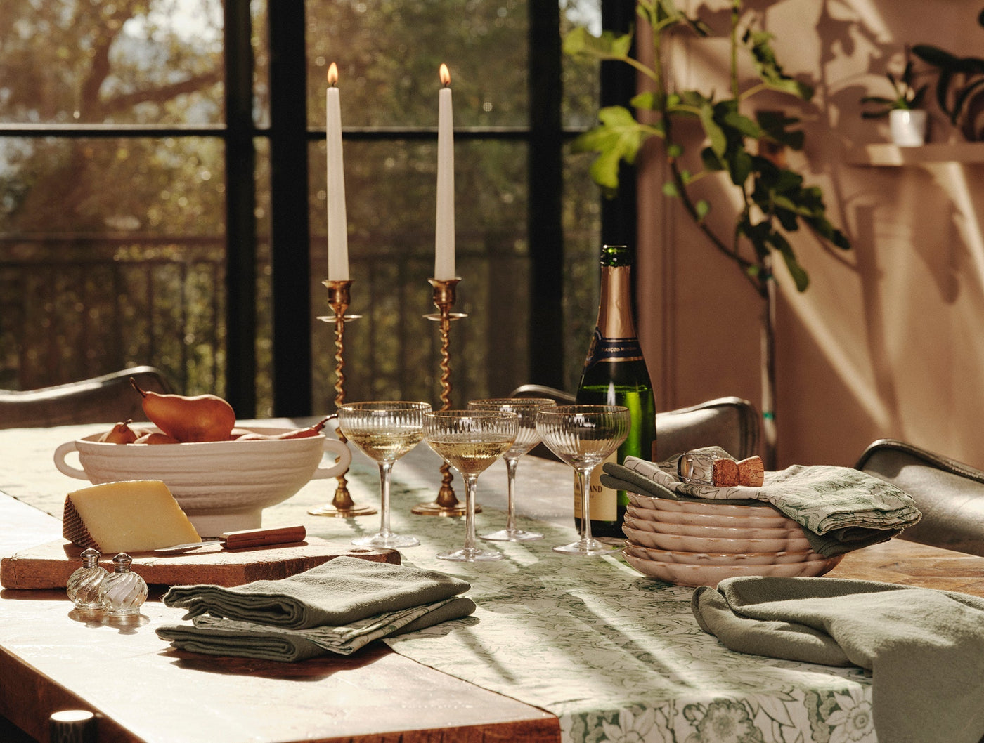 Sage green printed table runner styled with linen napkins, candles, and champagne on a dining table.