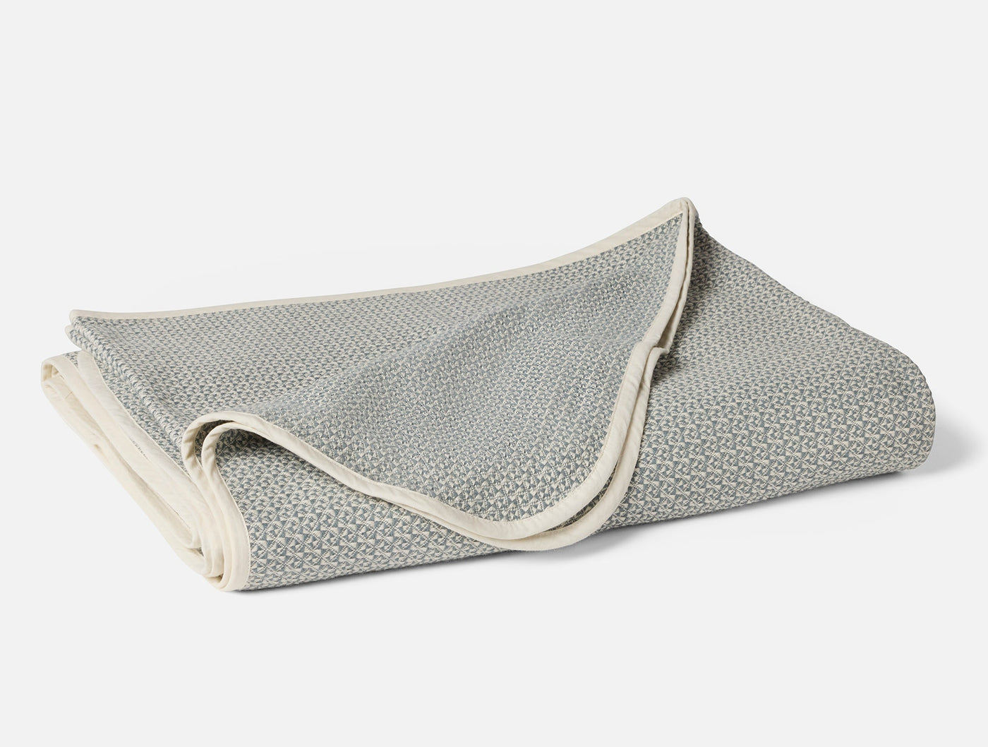 Close-up of folded Coyuchi Honeycomb blanket in sage with ivory binding trim.