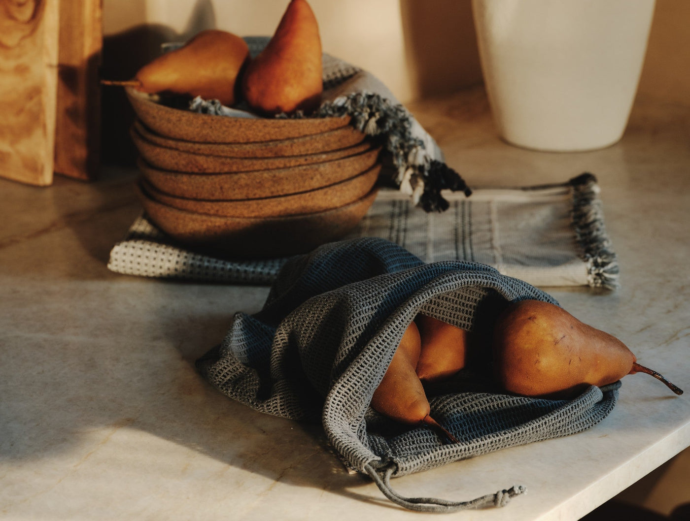 Coyuchi Conserve produce bag in slate blue waffle weave, filled with pears on a countertop.