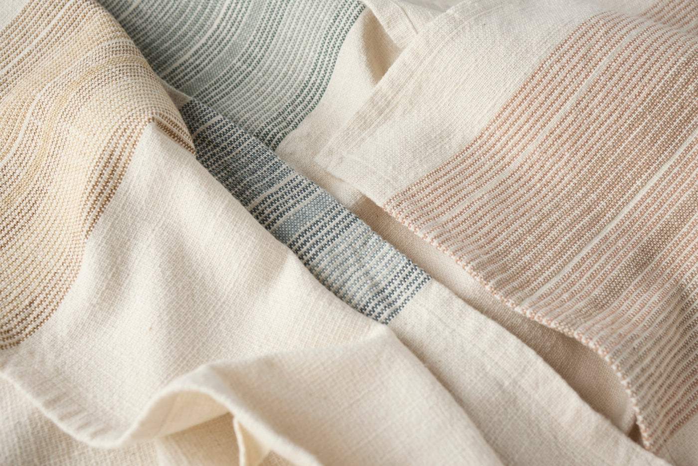 Close-up of Coyuchi Miraloma kitchen towels showing woven stripe details in sage, sand, and blush.