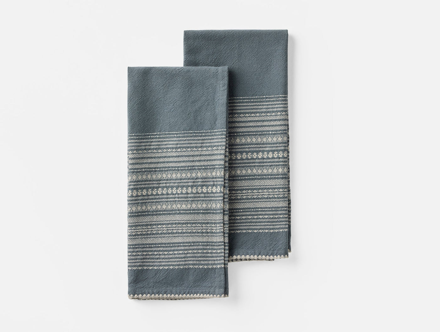 Two folded Coyuchi Oak hand towels in slate blue with woven stripe border detail.