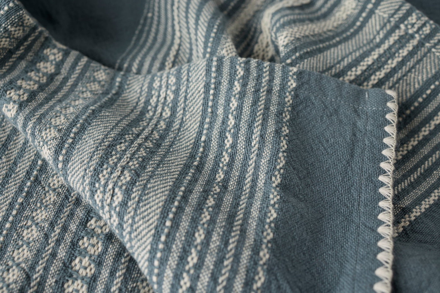 Close-up of Coyuchi Oak hand towel in slate blue, showing woven stripe pattern and scalloped hem detail.