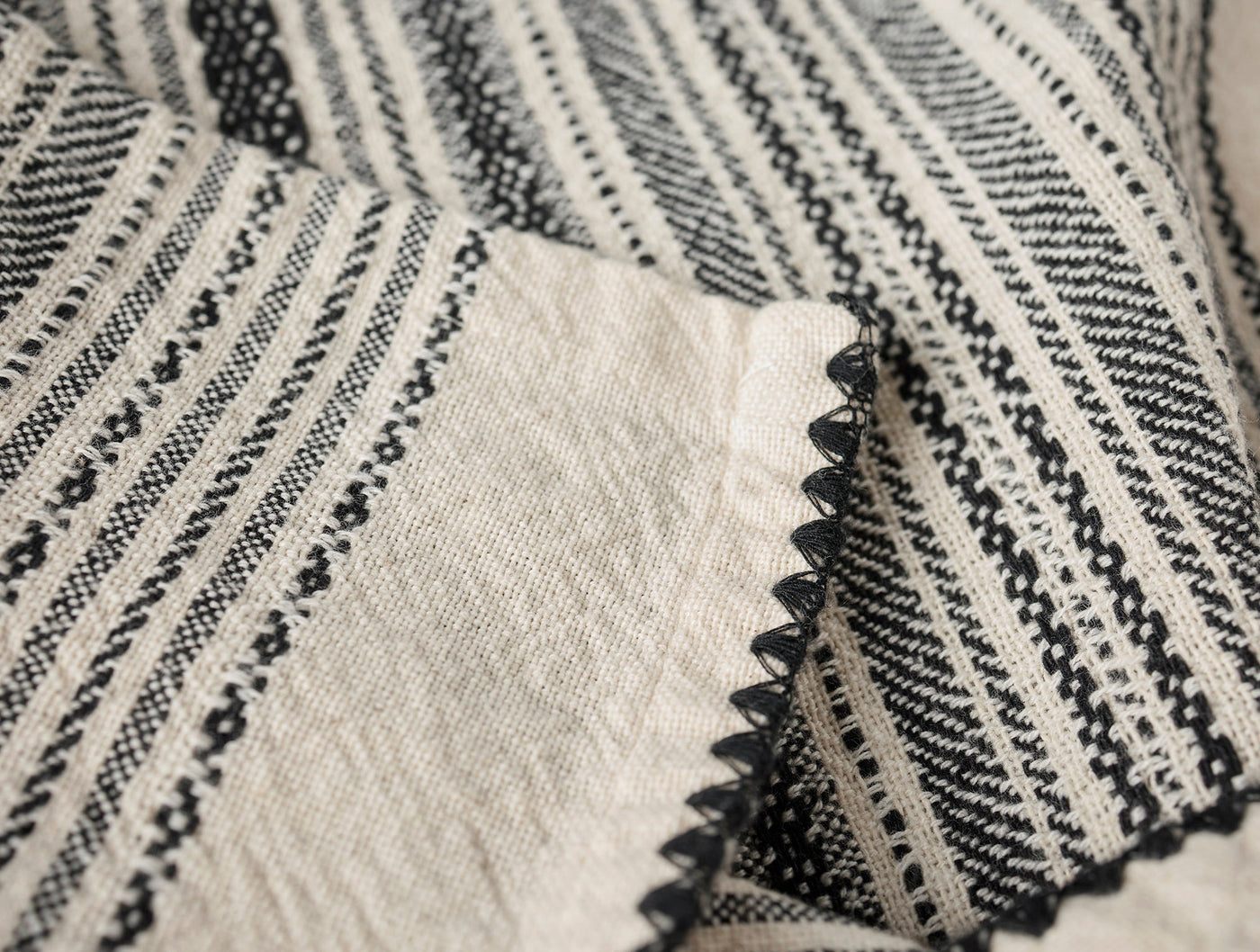 Close-up of Coyuchi Oak hand towel hem, black scalloped edge on ivory striped linen weave.