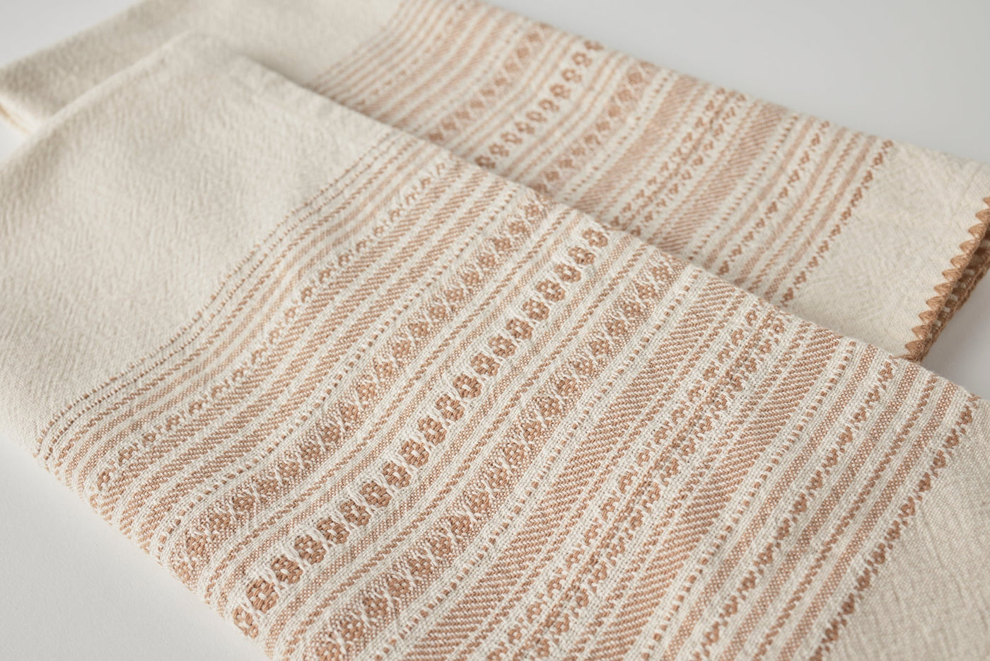 Close-up of Coyuchi Oak hand towels showing blush stripe and floral woven border detail.