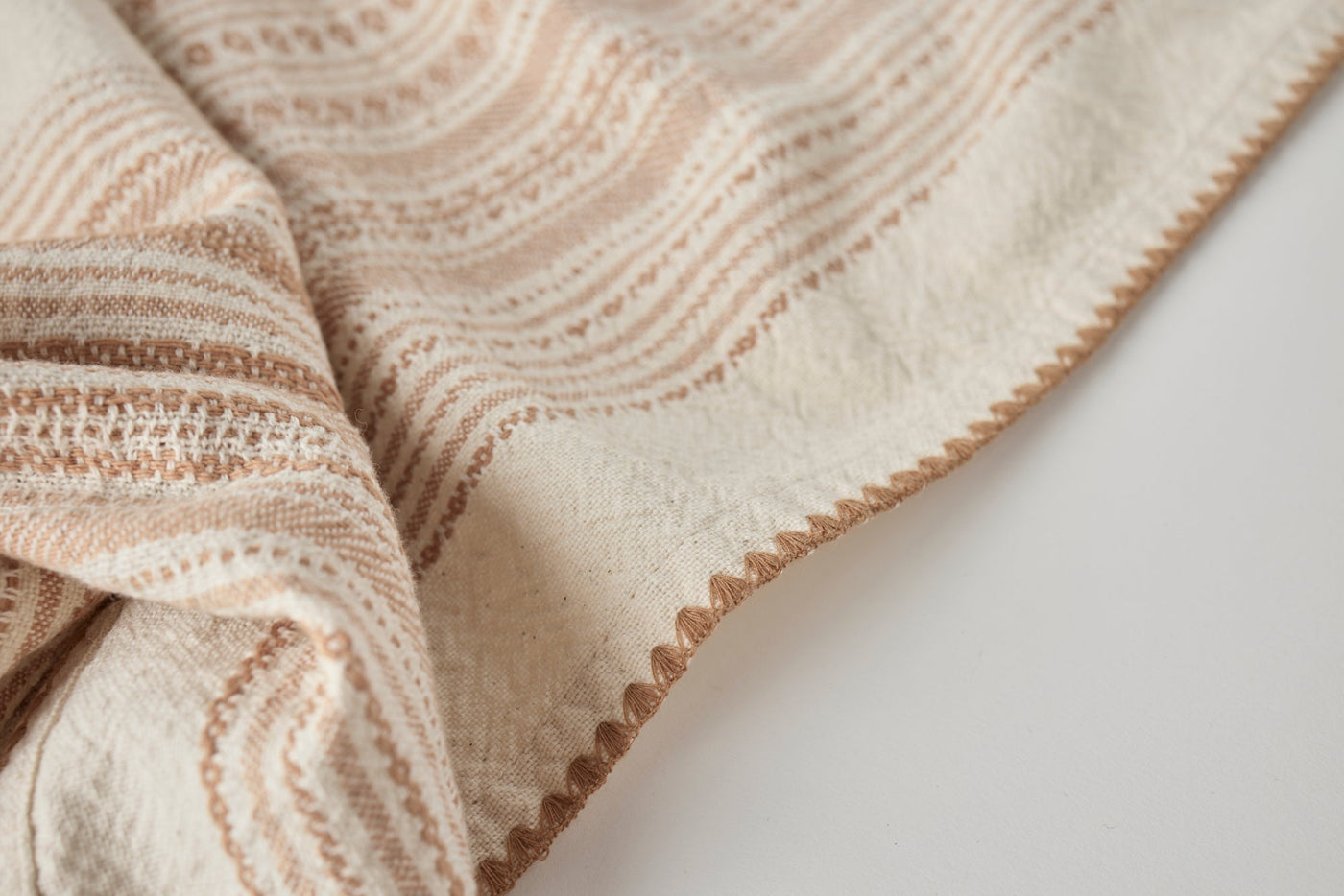 Close-up of Coyuchi Oak hand towel corner, ivory with terracotta wavy stripes and scalloped edge.
