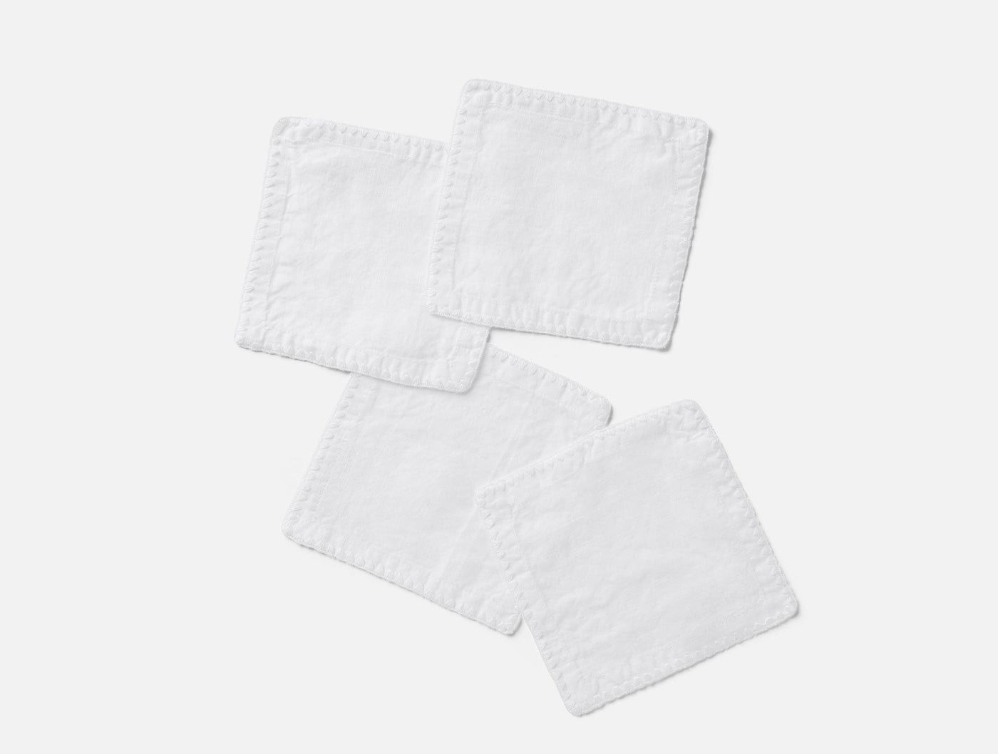 Four white linen napkins with embroidered edges arranged loosely on a light grey background.