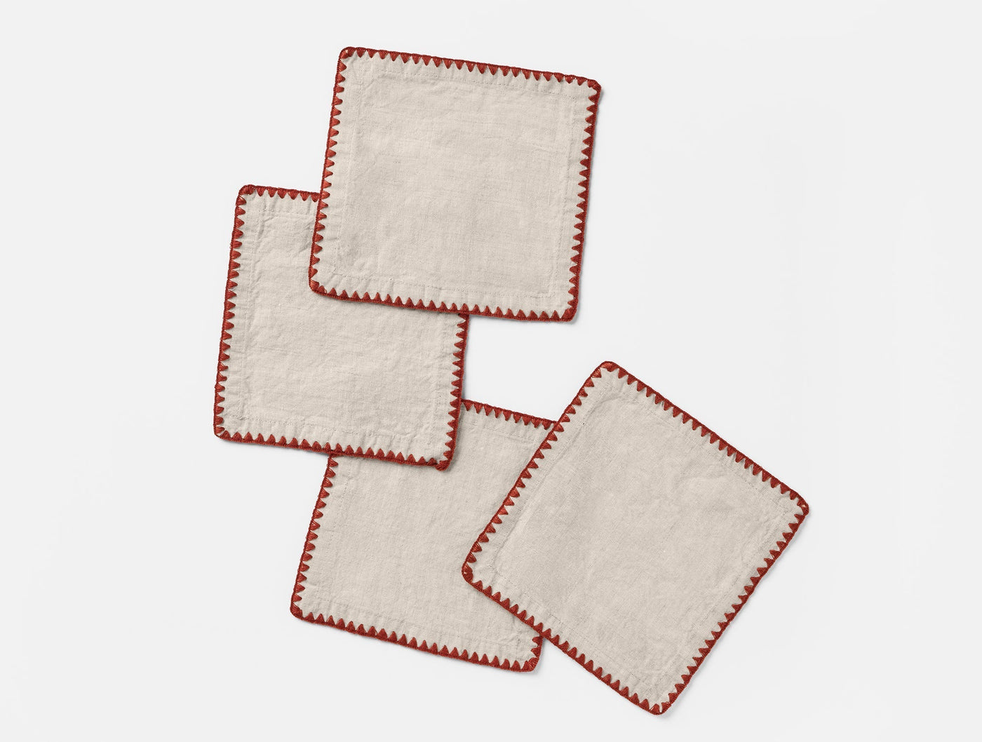 Four Coyuchi Olivos linen cocktail napkins, natural with red whipstitch trim, fanned flat.
