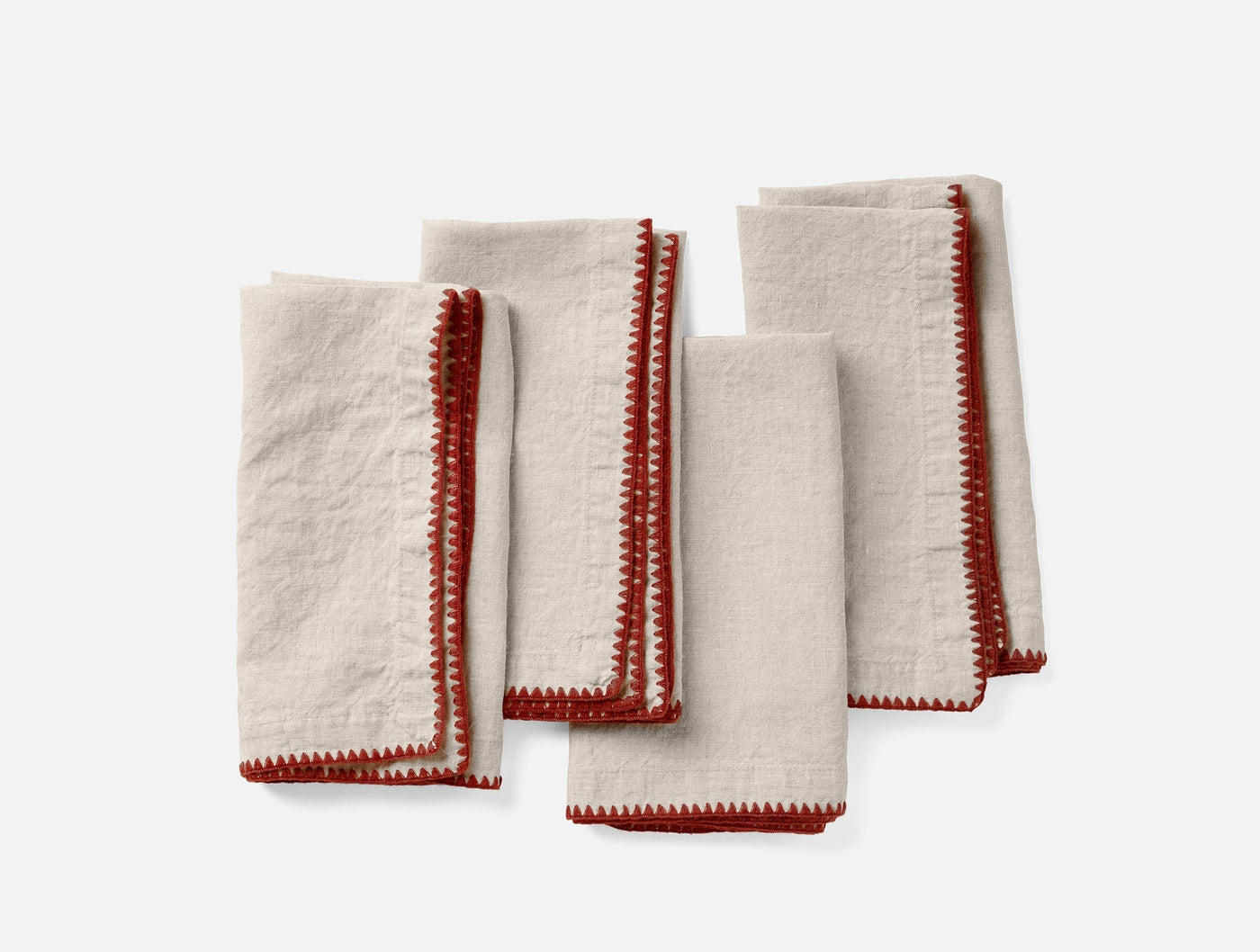 Close-up of four ivory linen napkins with red crochet-style embroidered edges, folded flat.