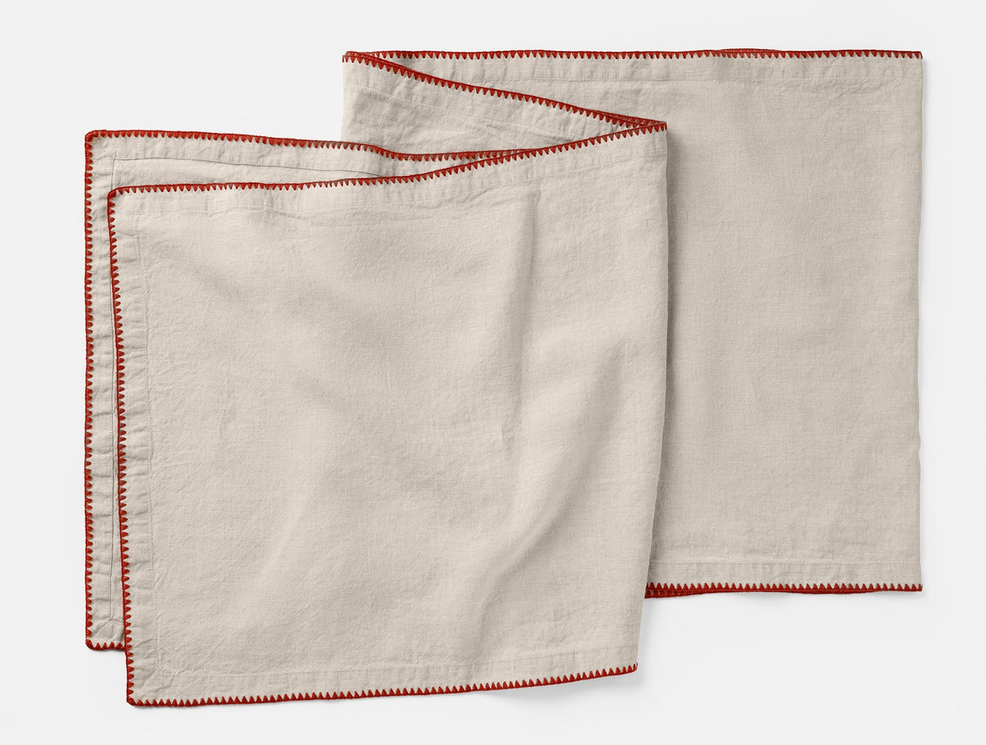 Three ivory linen napkins with red embroidered border stitching, fanned flat on white background.