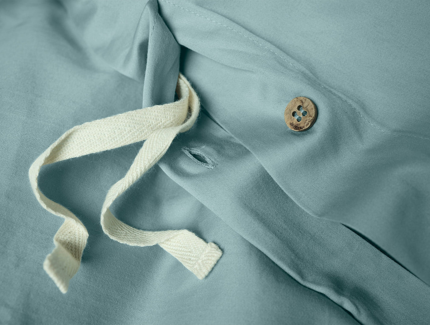 Close-up of seafoam sateen duvet cover interior ties and natural wood button closure.