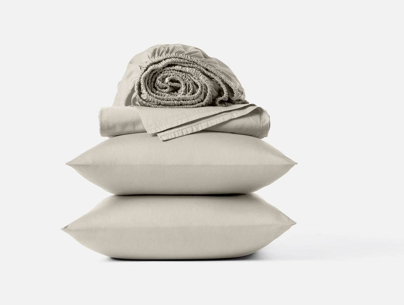 Close-up of stacked sand Coyuchi Cloud Soft Sateen pillowcases with rolled fitted sheet on top.