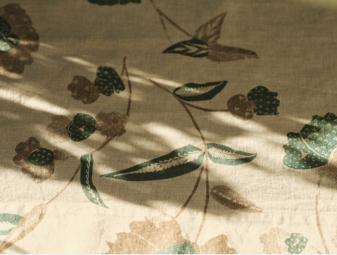 Close-up of Coyuchi Aurora Print table runner showing botanical floral and berry pattern in sage and brown.