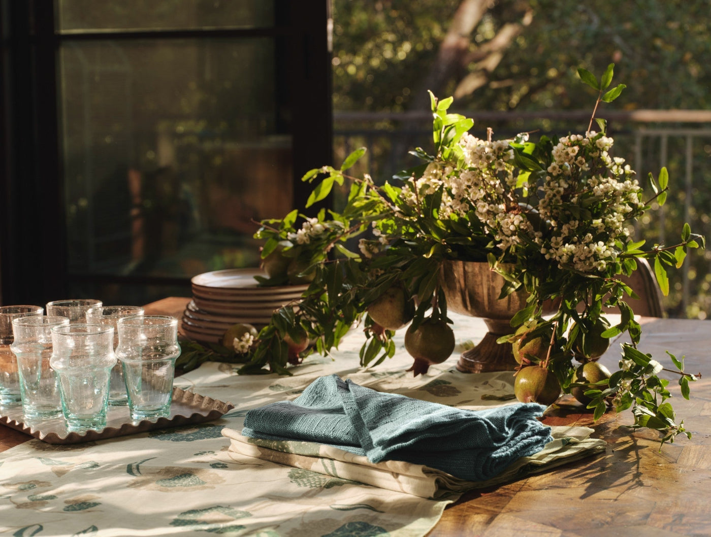 Teal linen napkins folded on a sunlit table with floral arrangement and glassware.
