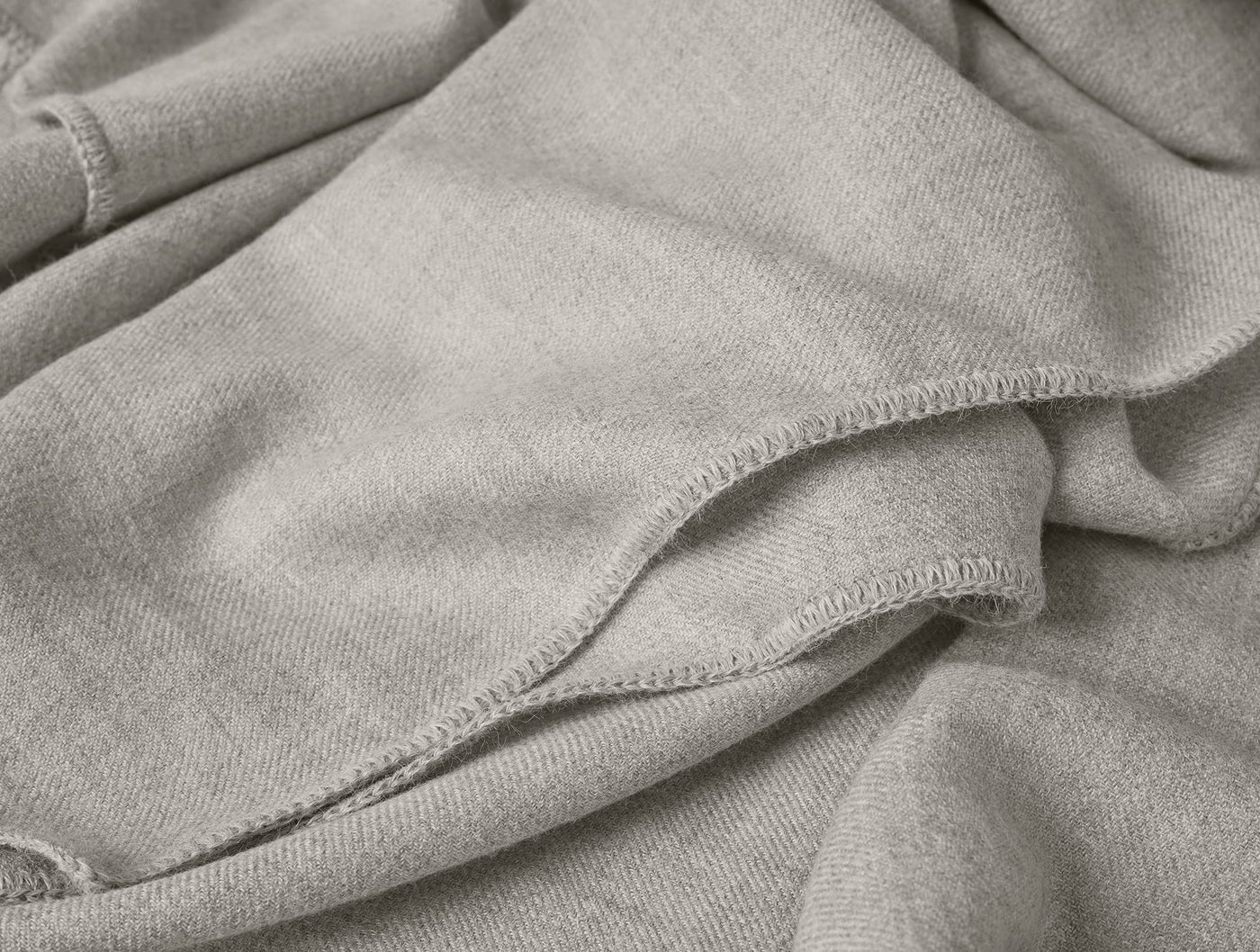 Close-up of Coyuchi Pacaya Baby Alpaca blanket hem, showing overlock stitching on greige fabric.