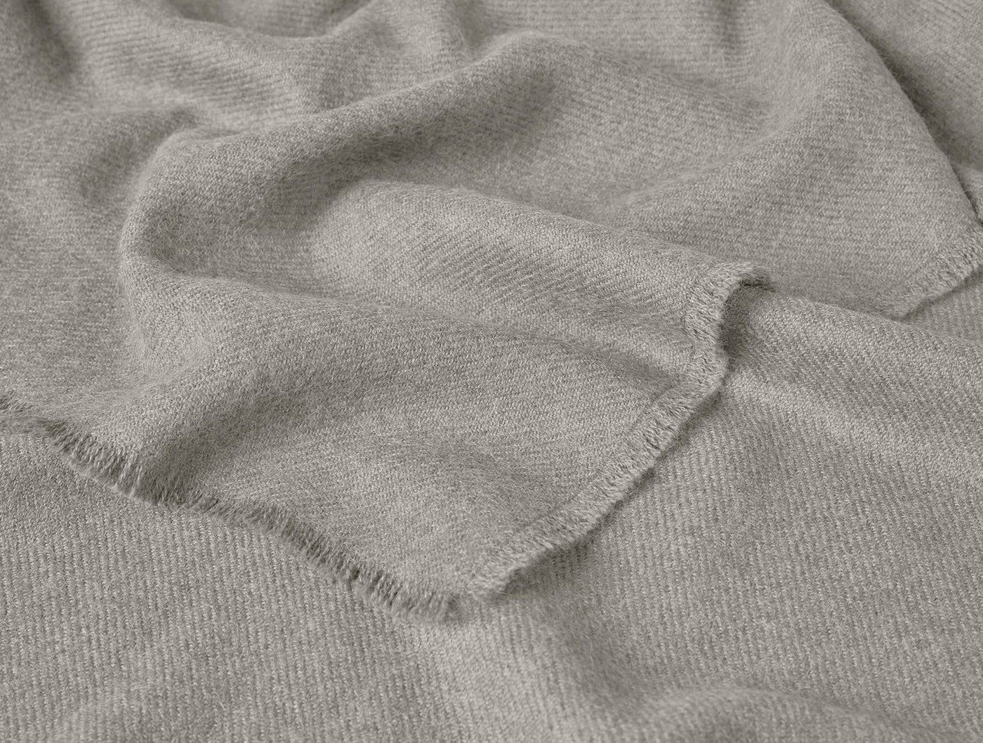 Close-up of fringed hem on draped Coyuchi Pacaya Baby Alpaca throw in warm grey.