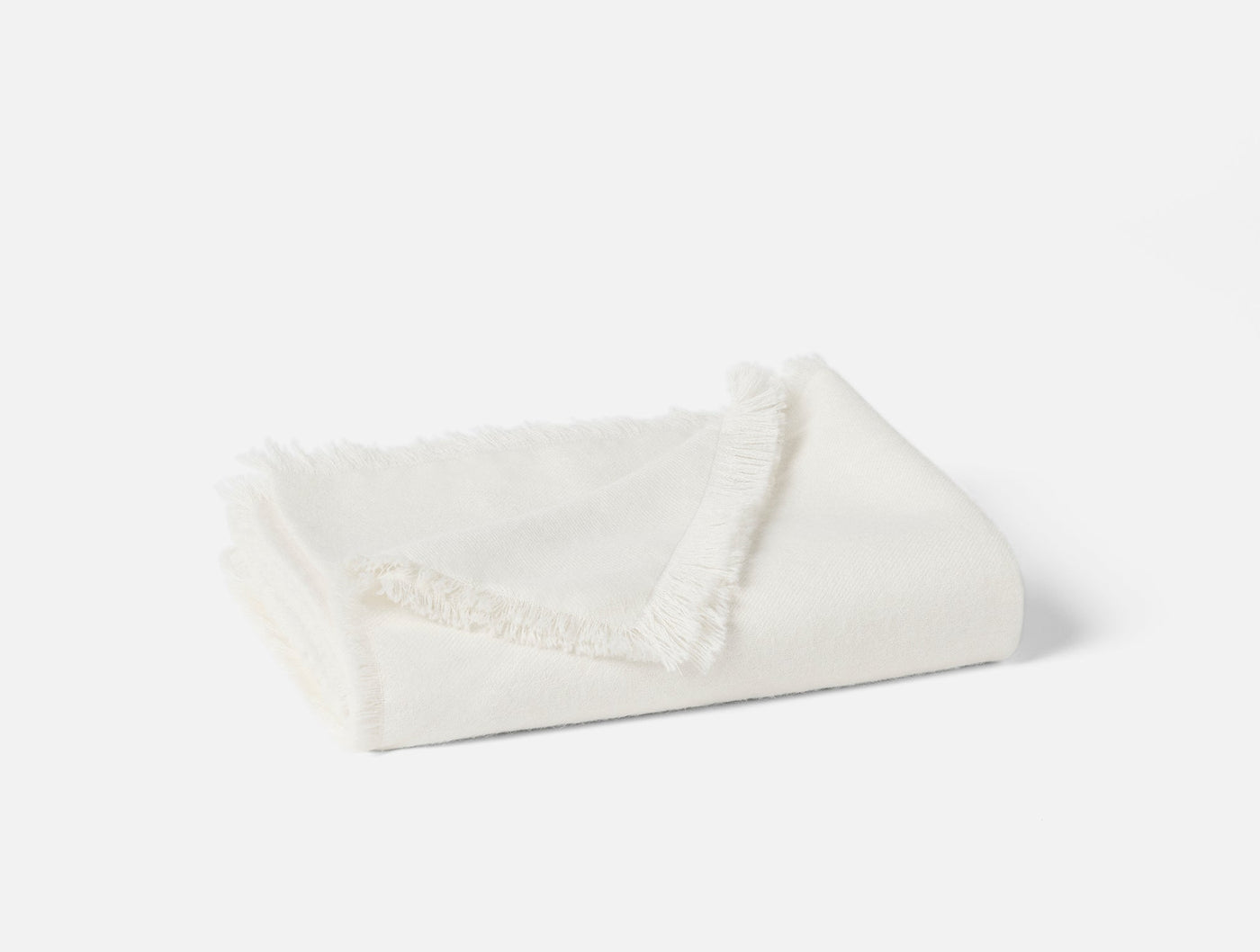 Folded ivory alpaca throw with delicate fringe trim, angled view on light background.