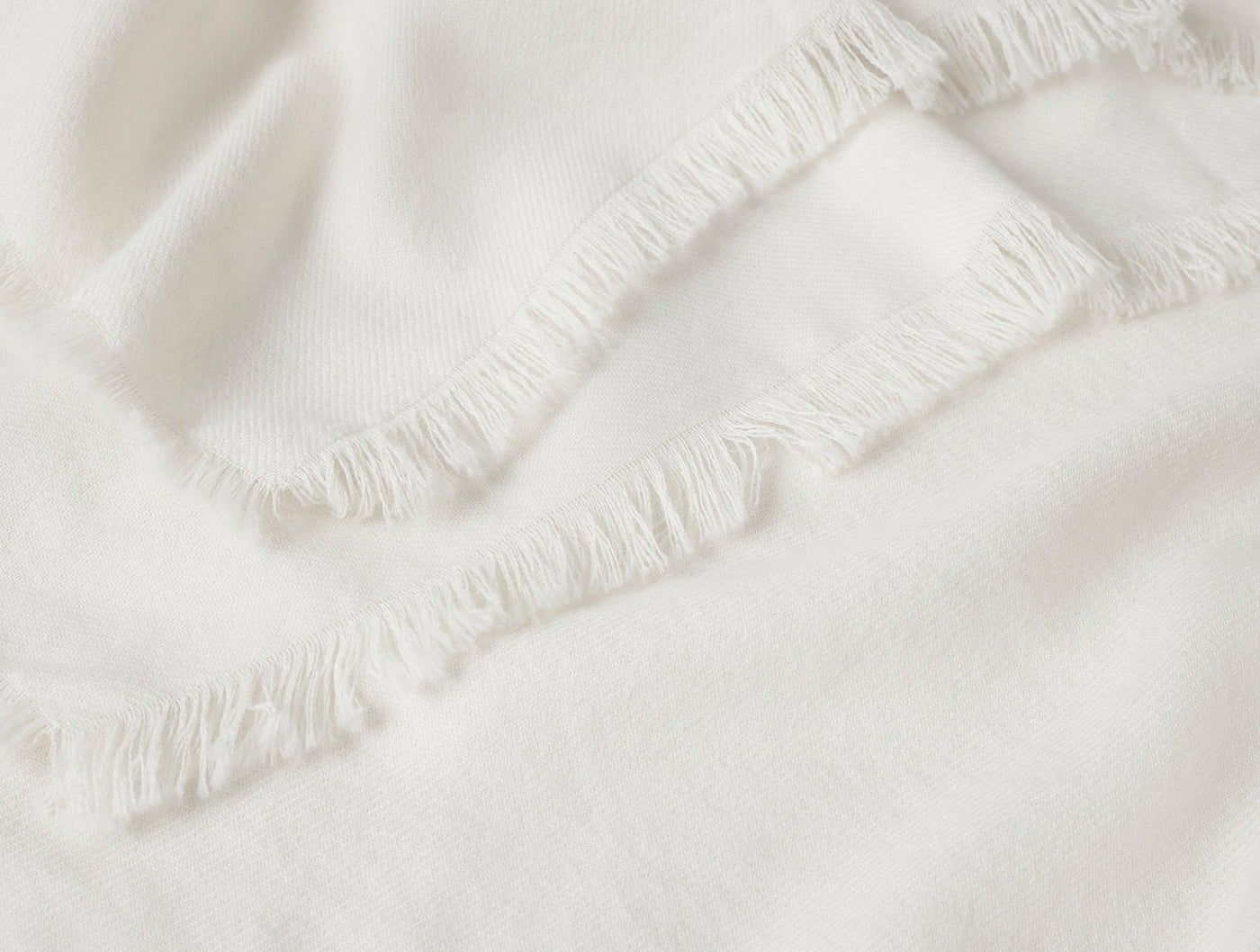 Close-up of ivory baby alpaca throw with delicate fringe trim and soft draping.