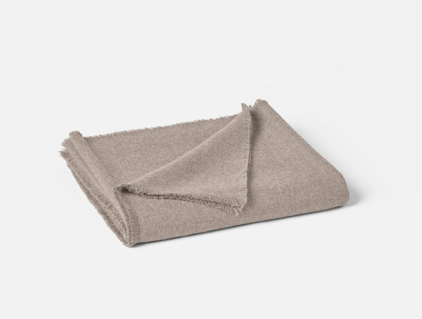 Folded taupe alpaca throw with fringe trim detail, soft textured weave visible at corner fold.