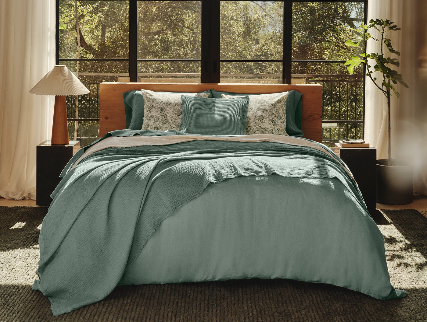 Coyuchi Topanga Matelassé blanket in sage green draped over styled bed near sunlit windows.