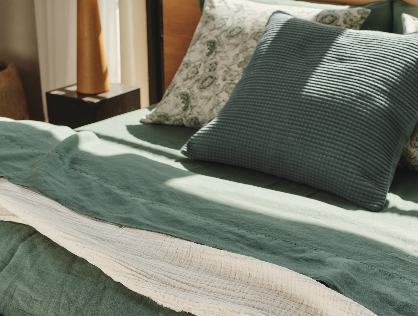 Close-up of sage green linen sheet set with waffle-knit pillow and floral accent pillow.