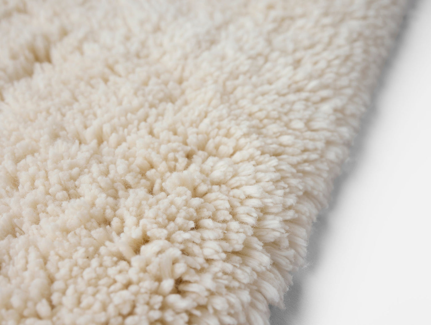 Close-up of ivory shag bath rug corner showing dense, looped pile texture.