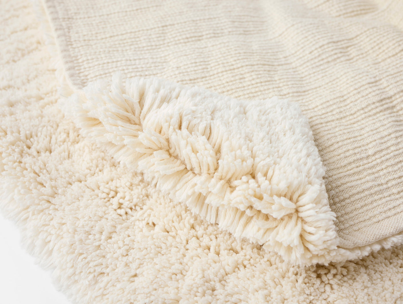 Close-up of ivory shag bath rug corner showing plush pile and woven ribbed reverse side.