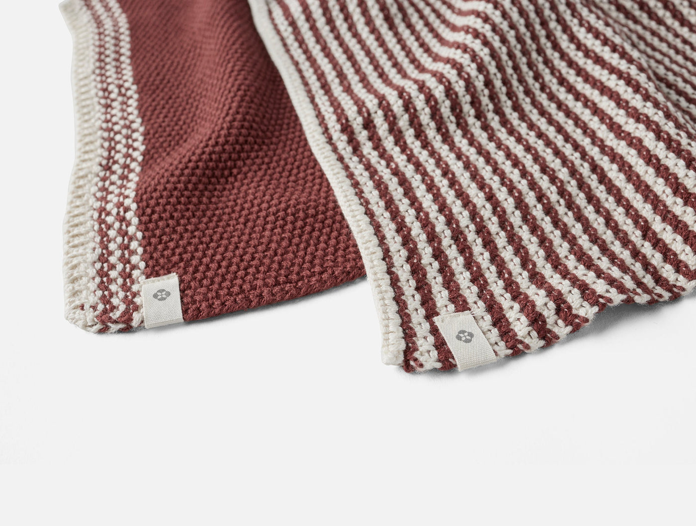 Close-up of Coyuchi Shasta dish cloths in rusty red, showing seed knit and stripe weave textures.