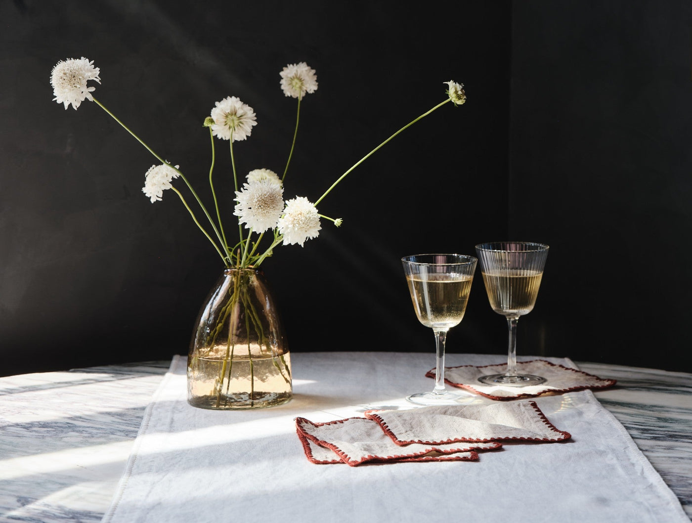 White linen table runner with red embroidered border, styled with wine glasses and florals.